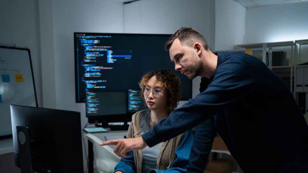 Man teaching a co-worker while pointing at a computer screen