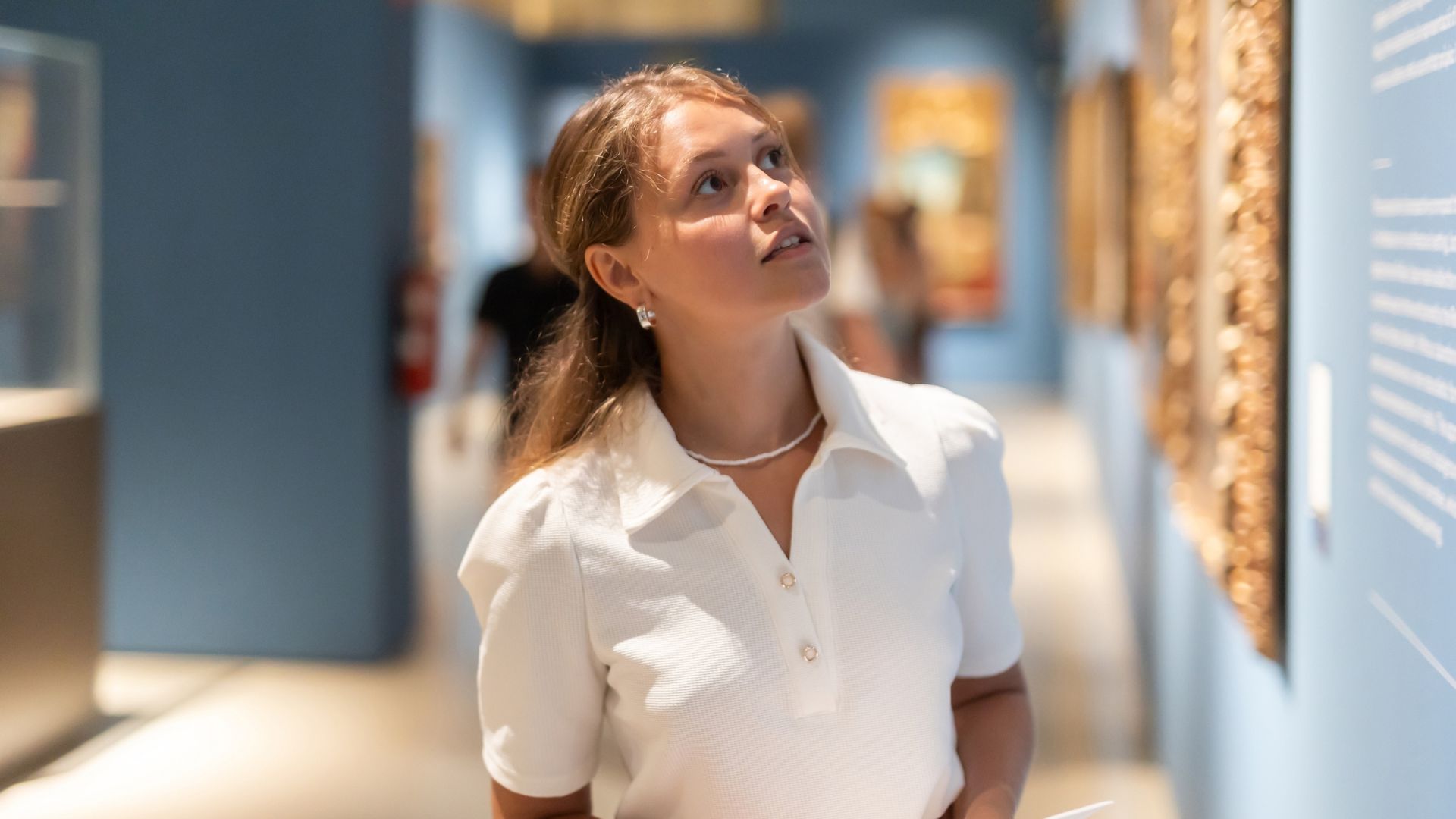 Portrait of young girl visitor with paper guide at the exhibition of paintings in the museum