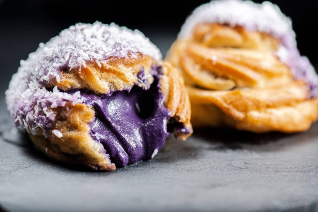 Ube cream puff with purple coloured white chocolate and coconut, also known as a Profiterole.