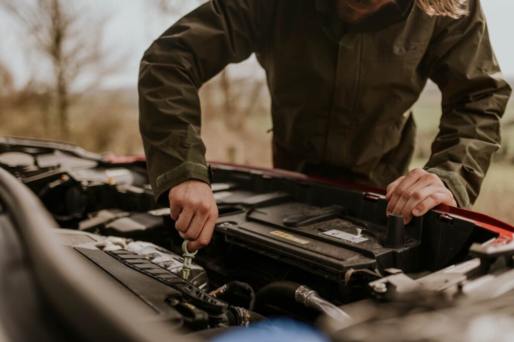Driver inspecting a vehicle engine bay during a winter safety check to help prevent breakdowns.