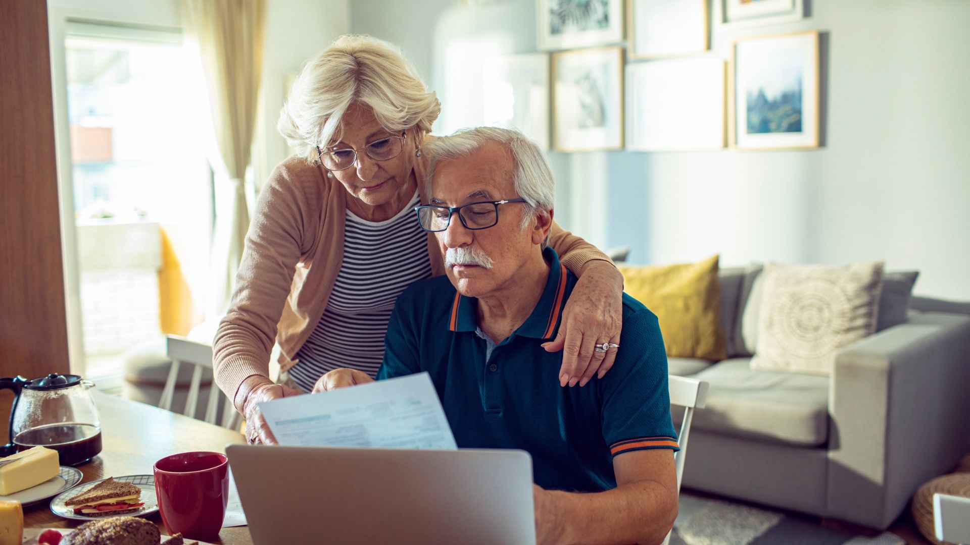 Worried senior couple reading bills with laptop at home