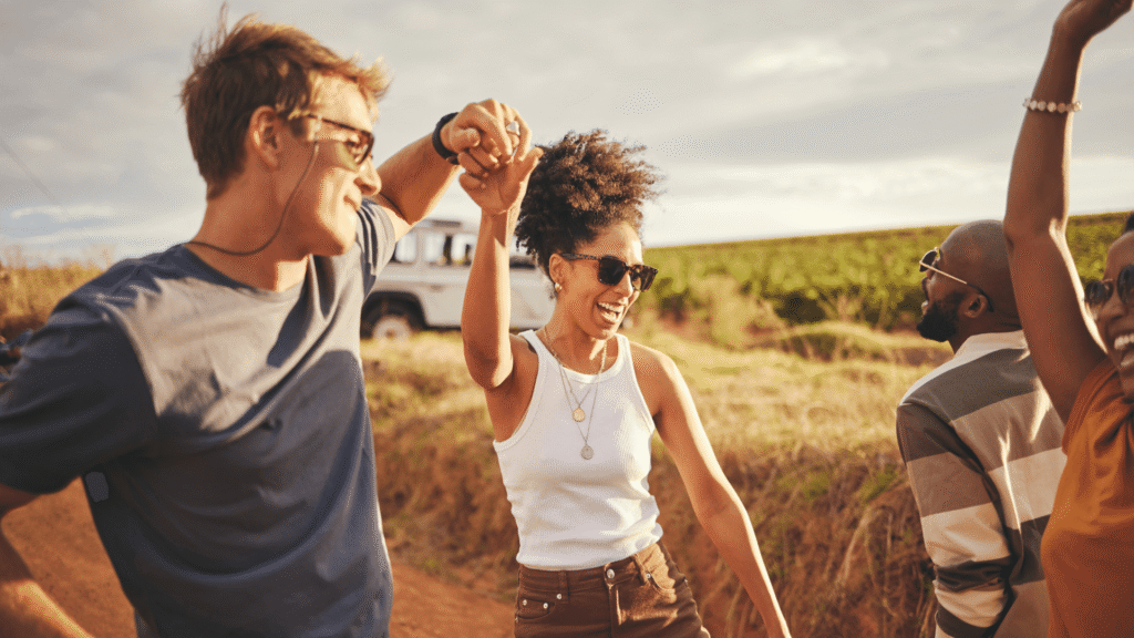 Friends, road trip and dance with a man and woman on a vacation, holiday or getaway in the dessert on a sand road. Travel, diversity and nature with a group of young people enjoying freedom outside