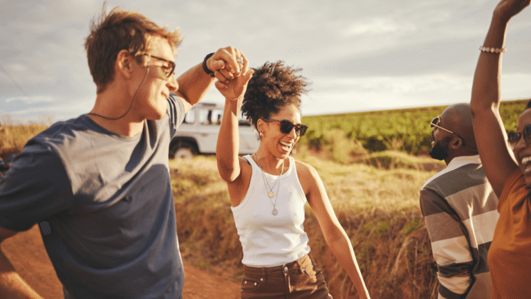 Friends, road trip and dance with a man and woman on a vacation, holiday or getaway in the dessert on a sand road. Travel, diversity and nature with a group of young people enjoying freedom outside