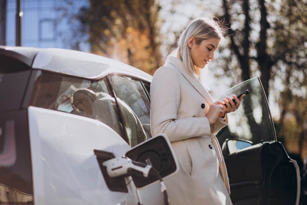 Woman using her phone next to a charging electric vehicle (EV).