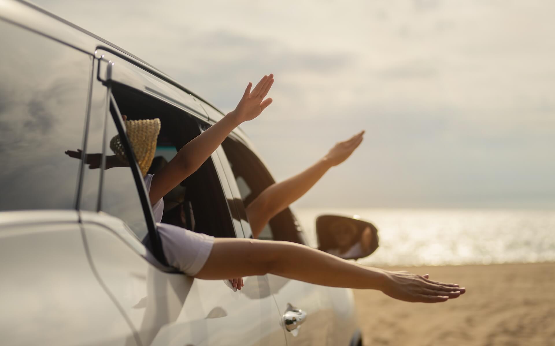 People extending their arms from a white SUV by the beach.