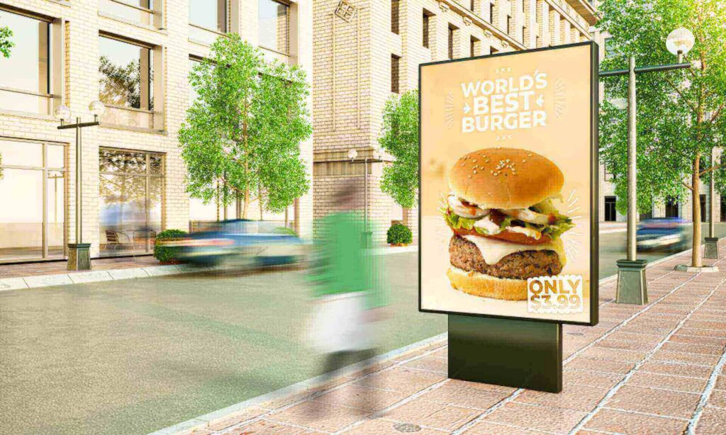 Digital billboard on a city sidewalk advertising a large burger with the text “World’s Best Burger – Only $3.99,” while pedestrians and cars blur past on the street.