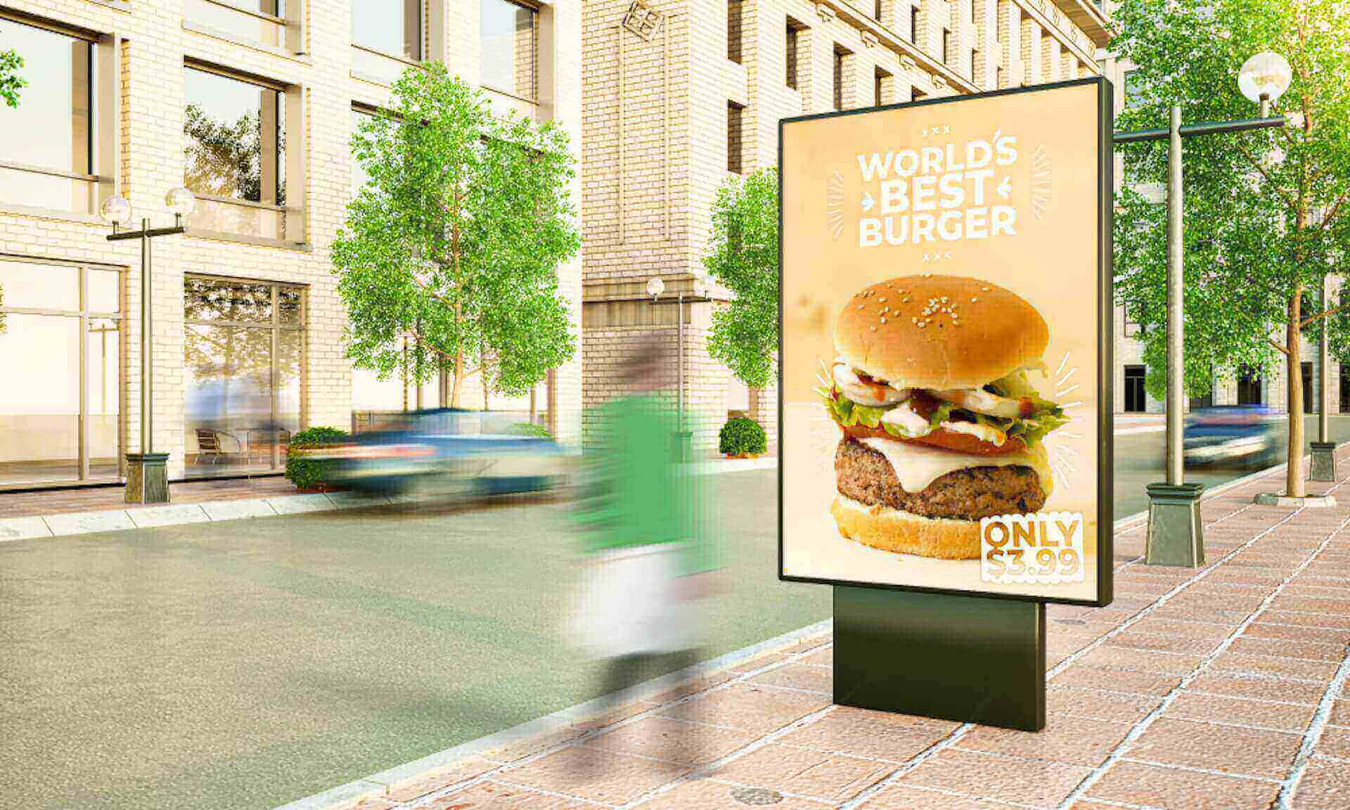 Digital billboard on a city sidewalk advertising a large burger with the text “World’s Best Burger – Only $3.99,” while pedestrians and cars blur past on the street.