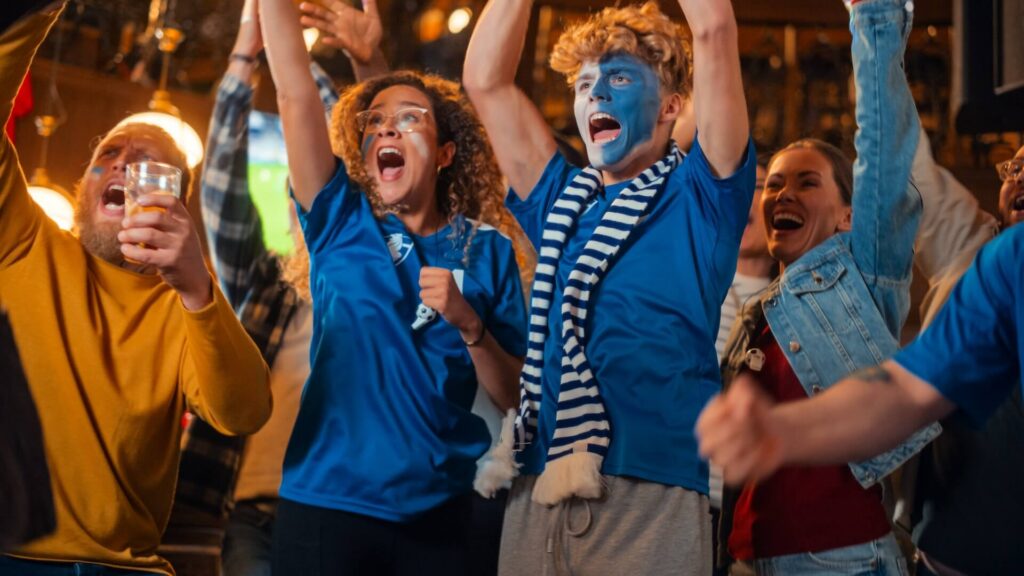Energetic group of young sports fans in blue shirts and face paint celebrating enthusiastically while watching a live game together.