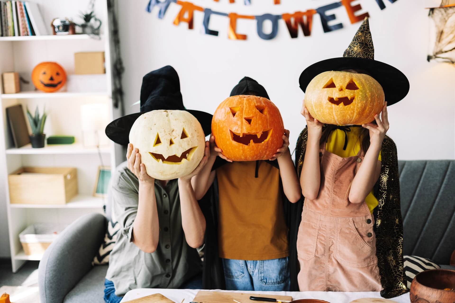 Family in witch hats and carved pumpkins, having fun at home for halloween.