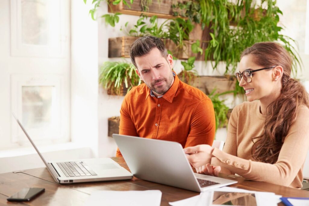 Shot of business people working together in the office. Beautiful young businesswoman sitting in front of laptop wtih his colleague and consulting about business. Teamwork.