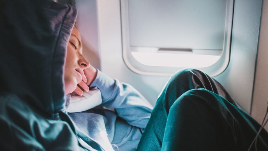 Tired blonde casual caucasian woman wearing sporty hoodie napping on seat while traveling by airplane. Commercial transportation by planes. Authentic image of real people