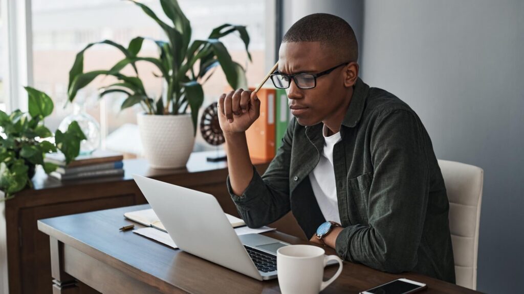 Laptop, idea and black man with doubt, confused or problem solving for software in creative startup. Computer, web designer and reading email for thinking, brainstorming or planning business decision