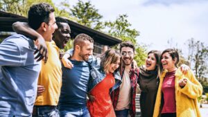 Seven friends, diverse in ethnicity, laugh and stand united in a park. Dressed in half-season clothing, they enjoy each other's company showing the true meaning of friendship beyond differences
