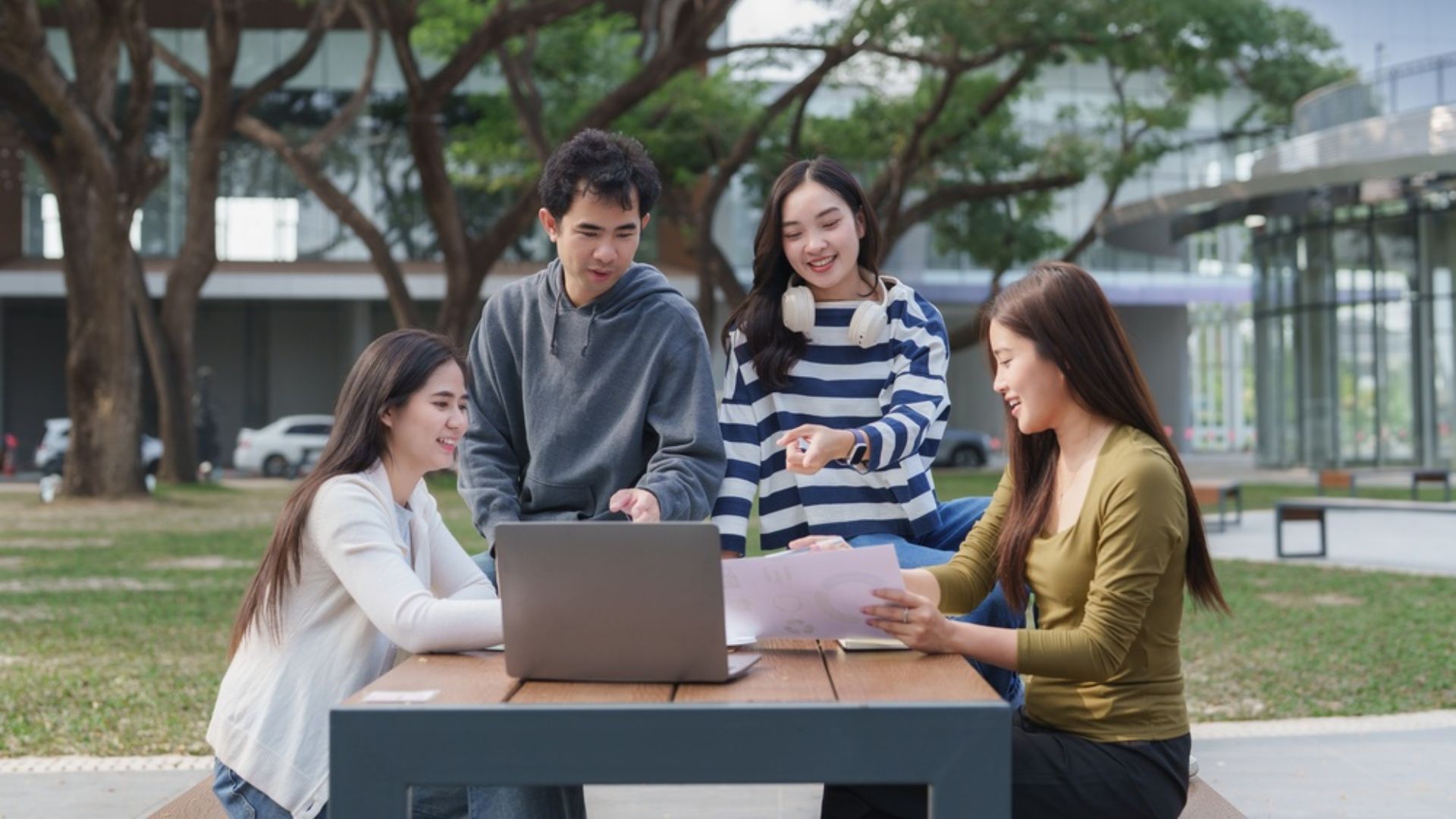 Four young asian students discussing ideas and working together on a laptop and documents at a table