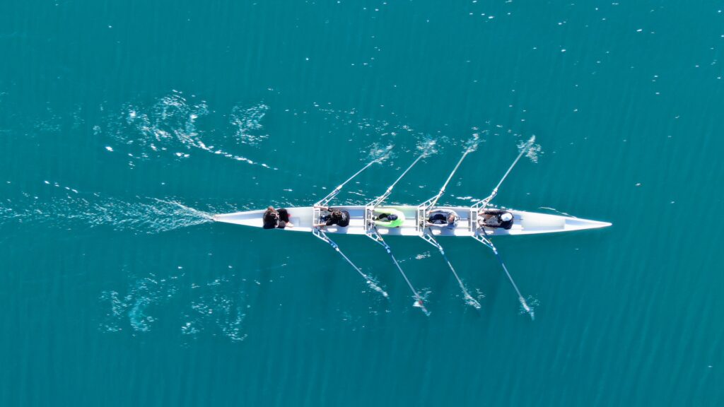 Aerial drone bird's eye view of sport canoe operated by team of young women in turquoise clear waters