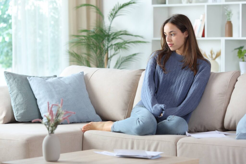 Pensive woman in blue thinking at home beside bills sitting on a sofa at home