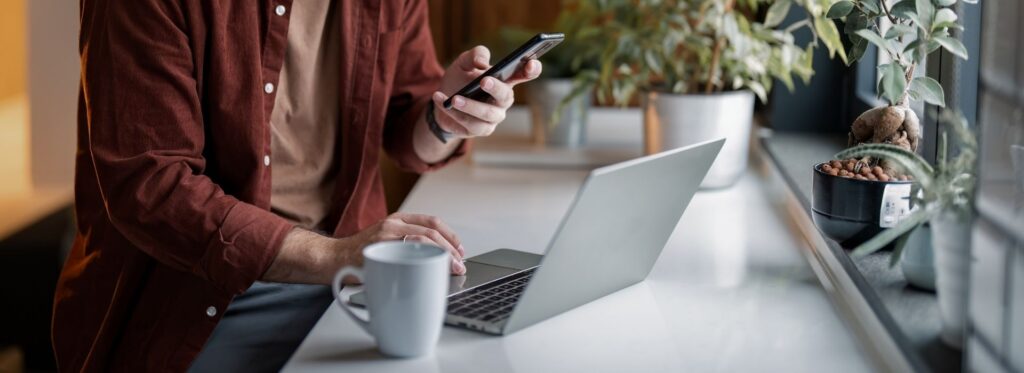 Person using phone and laptop at desk
