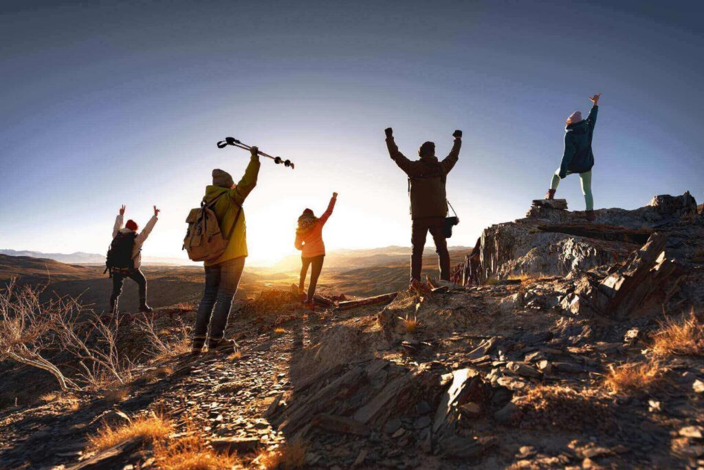 Five hikers celebrate on a mountain ridge at sunrise.