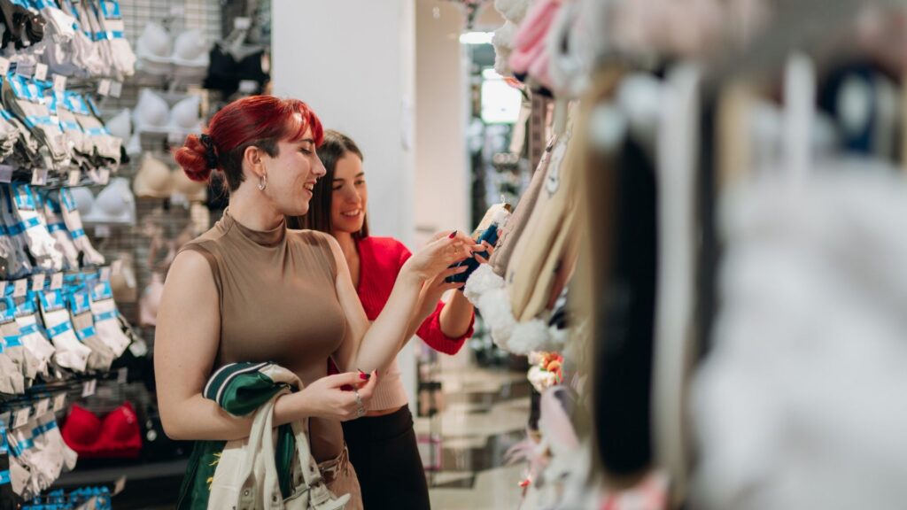 Two friends exploring apparel shelves in a retail shop, looking for personal clothing items