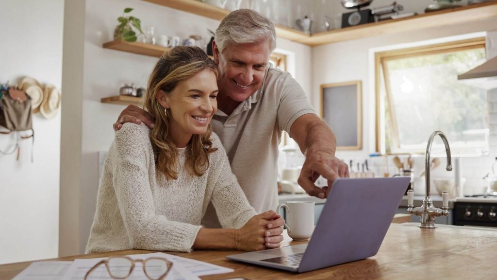 Couple using laptop together in kitchen.