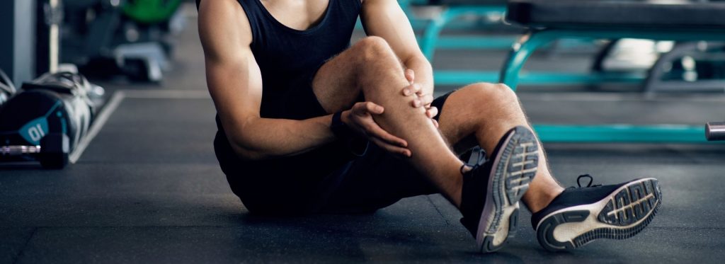 Man sits on floor holding injured leg.