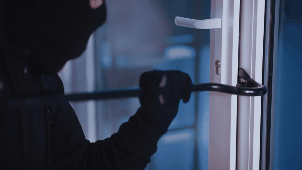 Vandalism Concept. Closeup of intruder wearing black balaclava and gloves breaking house door with crowbar
