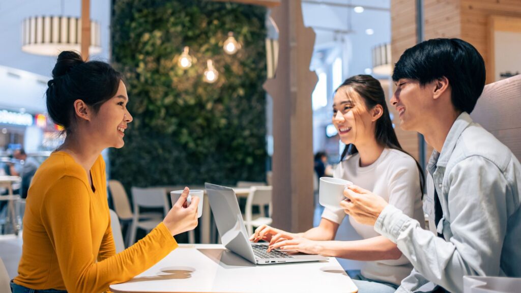 Group of Asian friends talking and using laptop computer in restaurant