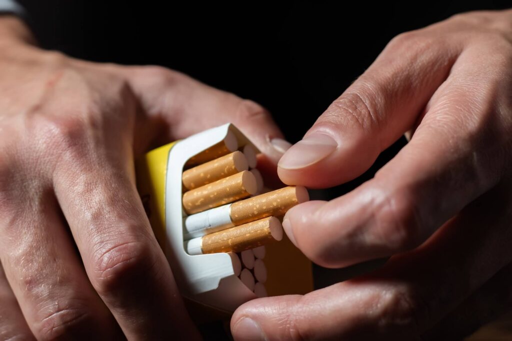 Close-up of a person’s hands opening a cigarette pack and pulling out a single cigarette