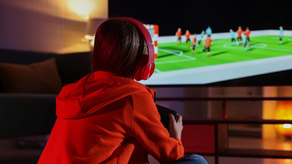 Little girl in headphones playing video game at home, back view
