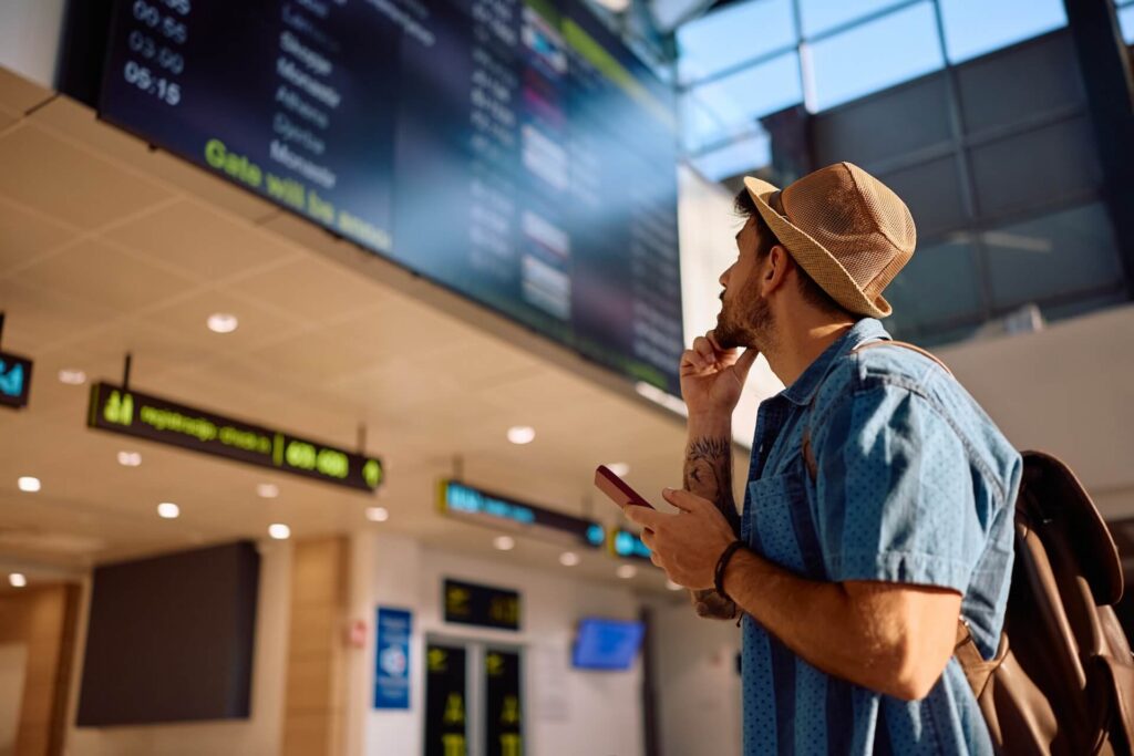 Male tourist checking flight departure on information board at the airport.