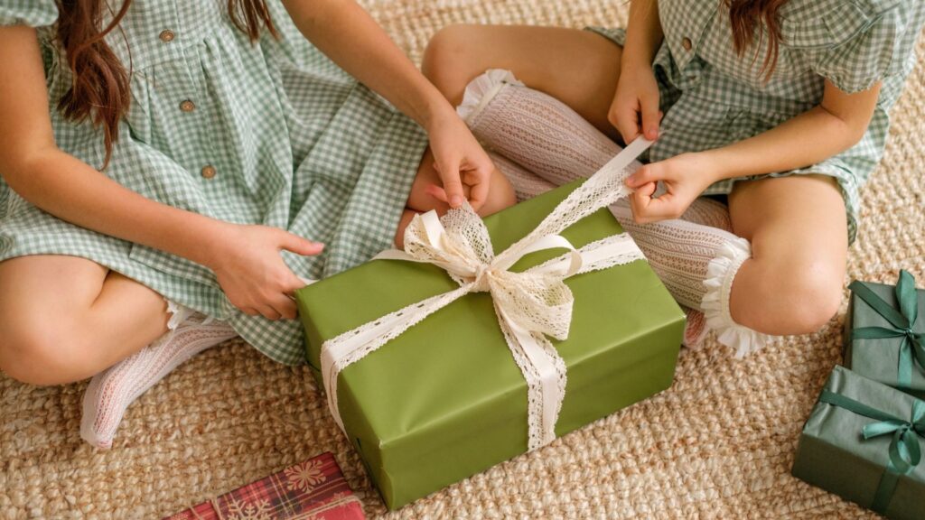 Children open a Christmas gift from Santa wrapped in green paper with a lace bow
