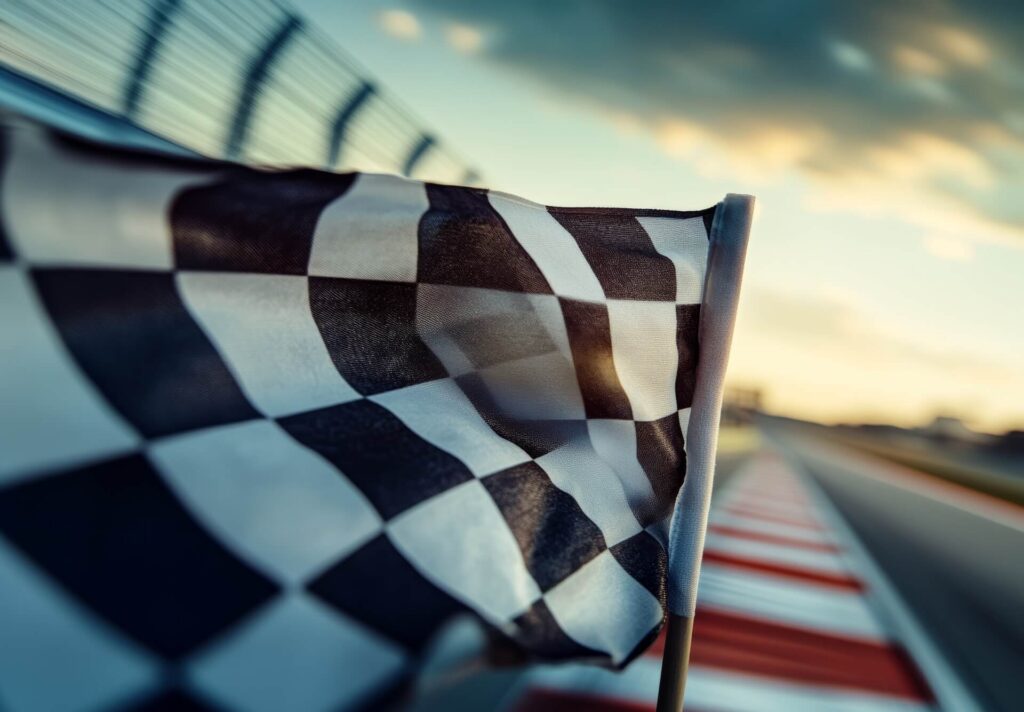 Checkered racing flag waving beside a racetrack at sunset.
