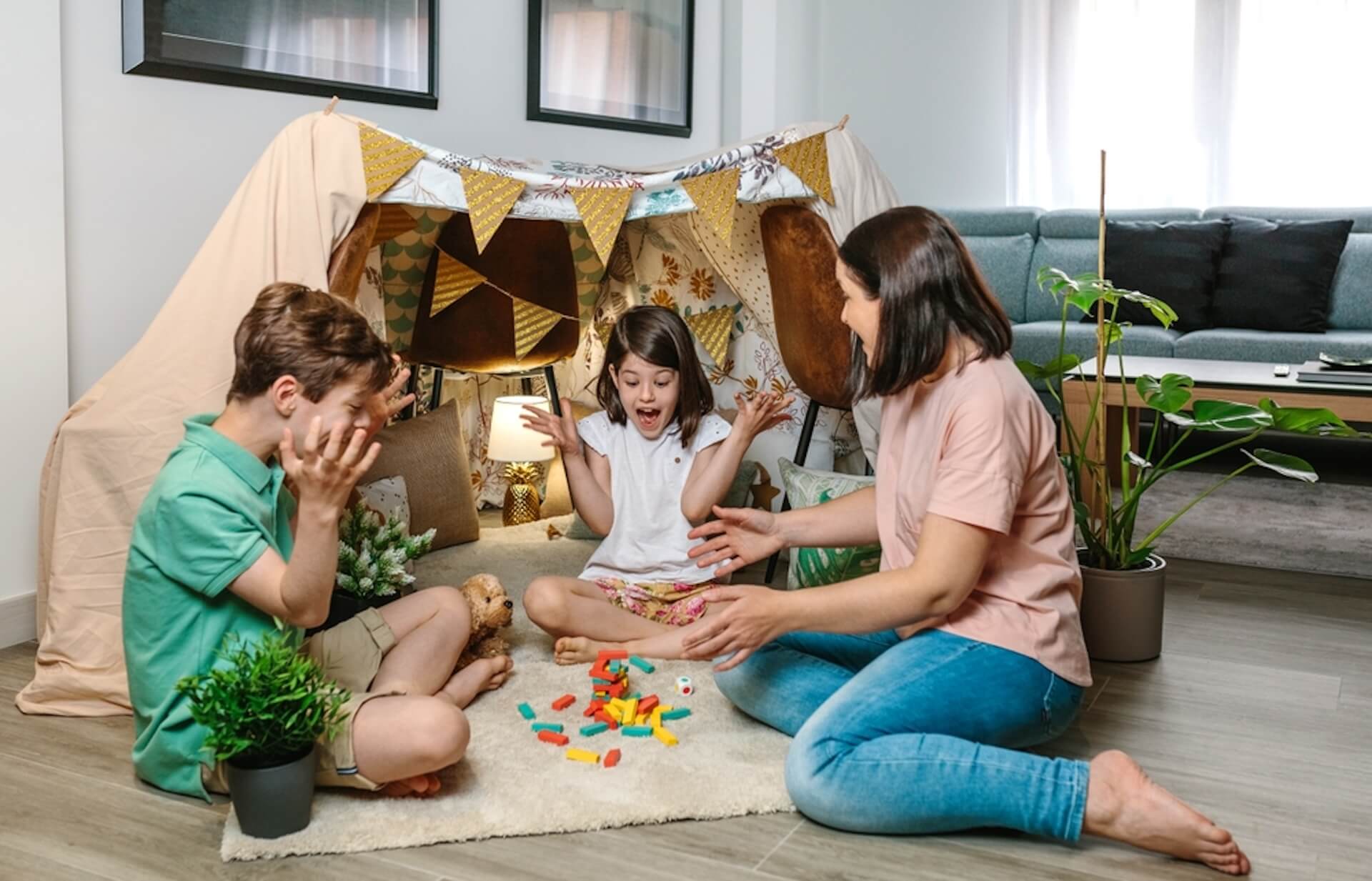 Family playing a game in a cozy blanket fort in a living room.
