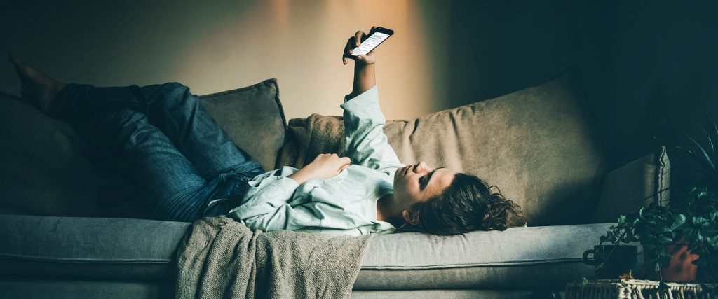 woman looking at her phone lying on a sofa a sign of survey fatigue