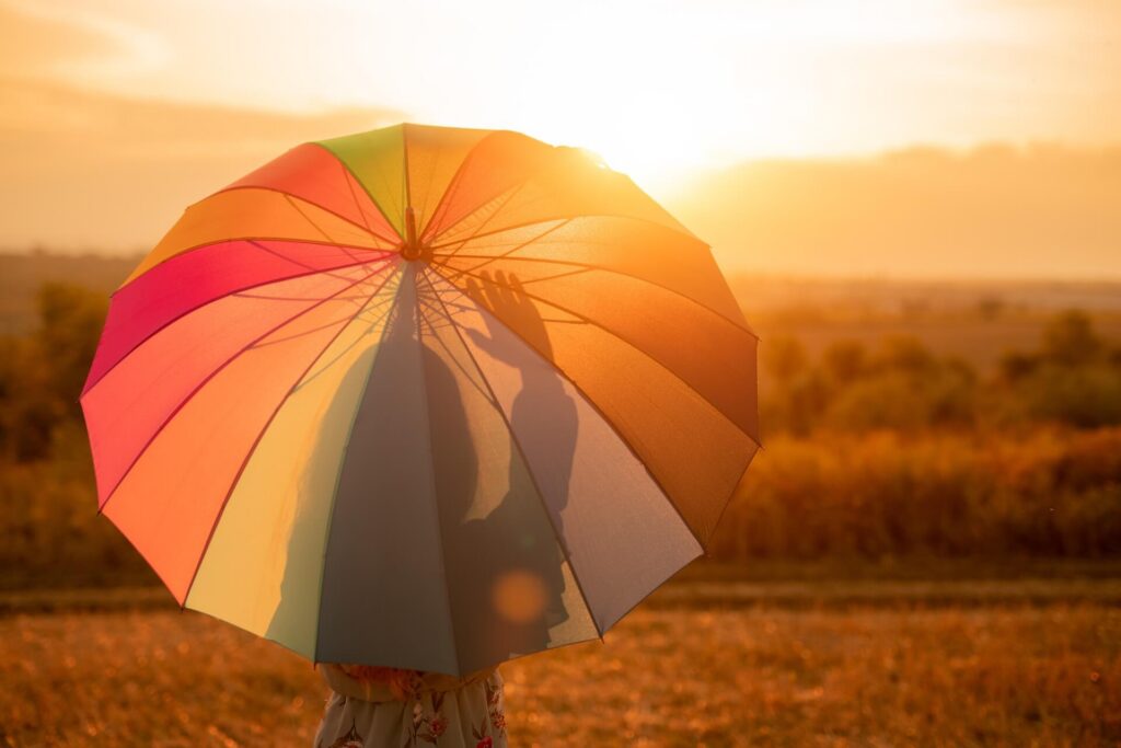 Back view of unrecognizable female with colorful umbrella admiring sunset and waving hand