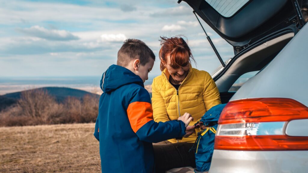 Mother and son take break from driving sitting by the car while drinking tea in nature.