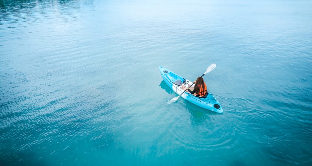 Woman kayaking isolatedly in the middle of the blue ocean