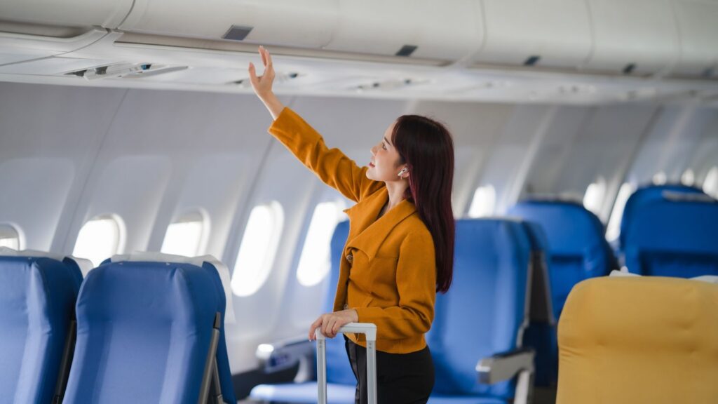 Asian traveler stowing luggage in overhead compartment
