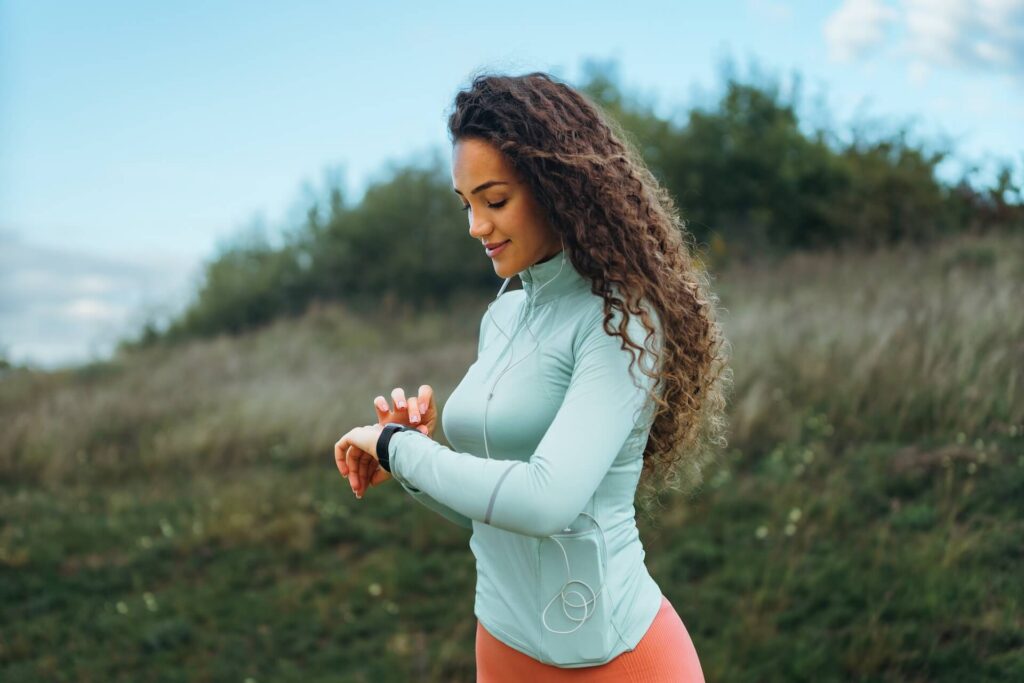 A fitness girl is looking at her smart watch to see how many steps she has been taking, as well as her pulse rate.