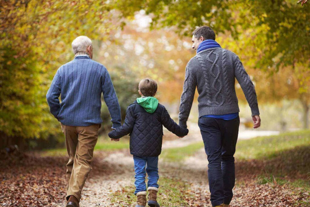 Three generations of a family walking along a tree-lined path during autumn.