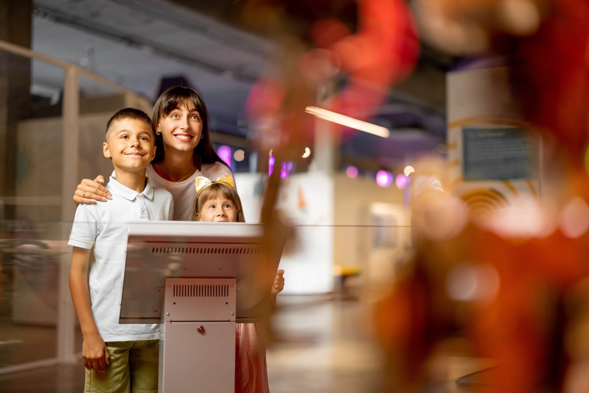 A mother and two children stand together at an interactive exhibit in a museum, smiling and looking at a display screen.